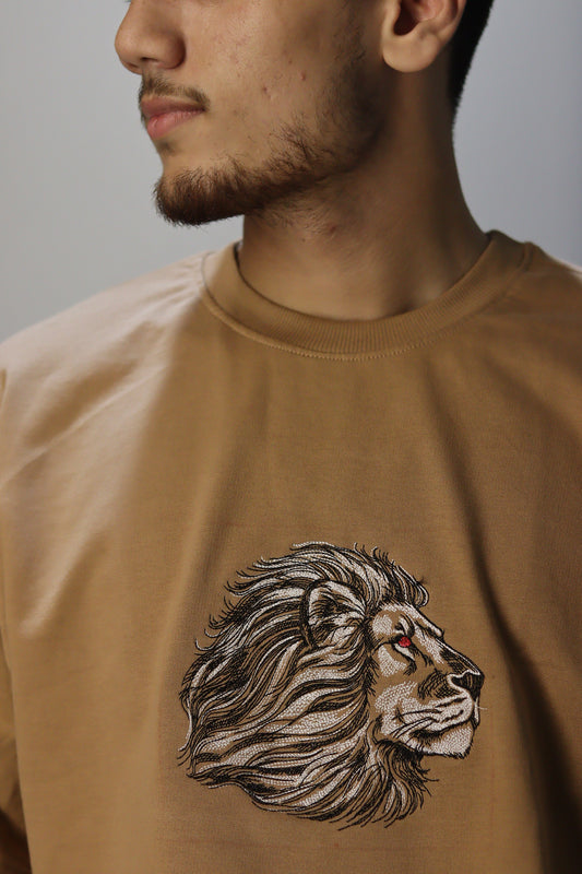 Man wearing a brown t-shirt with an embroidered design of a face with hair.